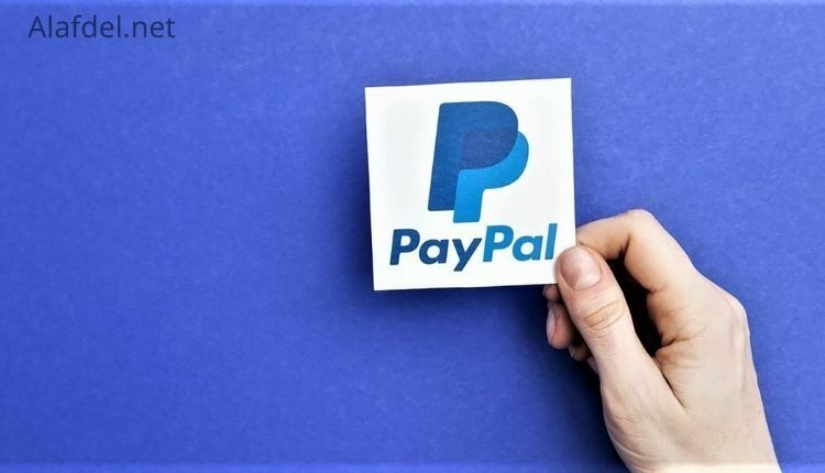 صورة بها كلمة باي بال بالإنجليزية PayPal على ورقة مربعة يمسكها يد إنسان وذلك ضمن مميزات حساب باي بال