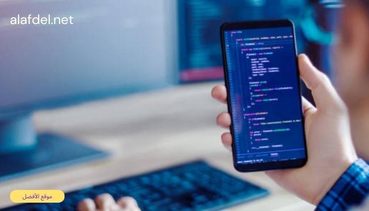 صورة بها شخص جالس أمام كمبيوتر وممسك بهاتف في يديه وذلك ضمن الحديث عن أنواع تطبيقات الجوال