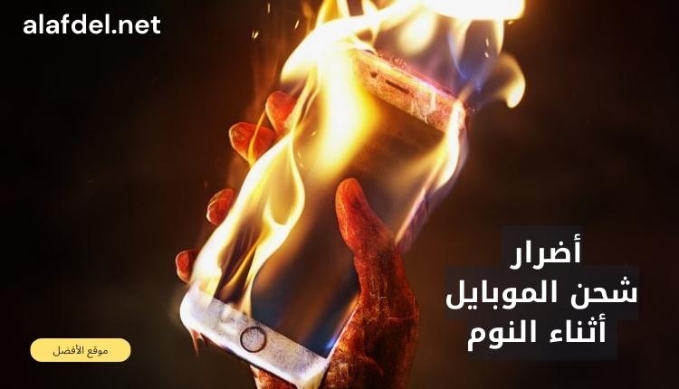 صورة بها يد تسمك هاتف يحترق للتعبير عن أضرار شحن الموبايل أثناء النوم The damages of charging the mobile phone while sleeping