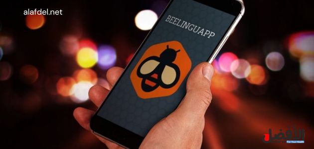 صورة بها يد تمسك هاتف ذكي موجود على شاشته شعار تطبيق Beelinguapp، والذي هو من افضل التطبيقات لتعلم اللغة الانجليزية